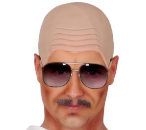 Kuvassa on lähikuva miehen kasvoista, joilla havainnollistetaan kaljumyssyn käyttöä. Hänellä on päässään ihonvärinen, lateksinen kaljumyssy, joka peittää hiukset kokonaan ja luo otsalle realistisia ihopoimuja. Asukokonaisuutta täydentävät pilottimalliset 